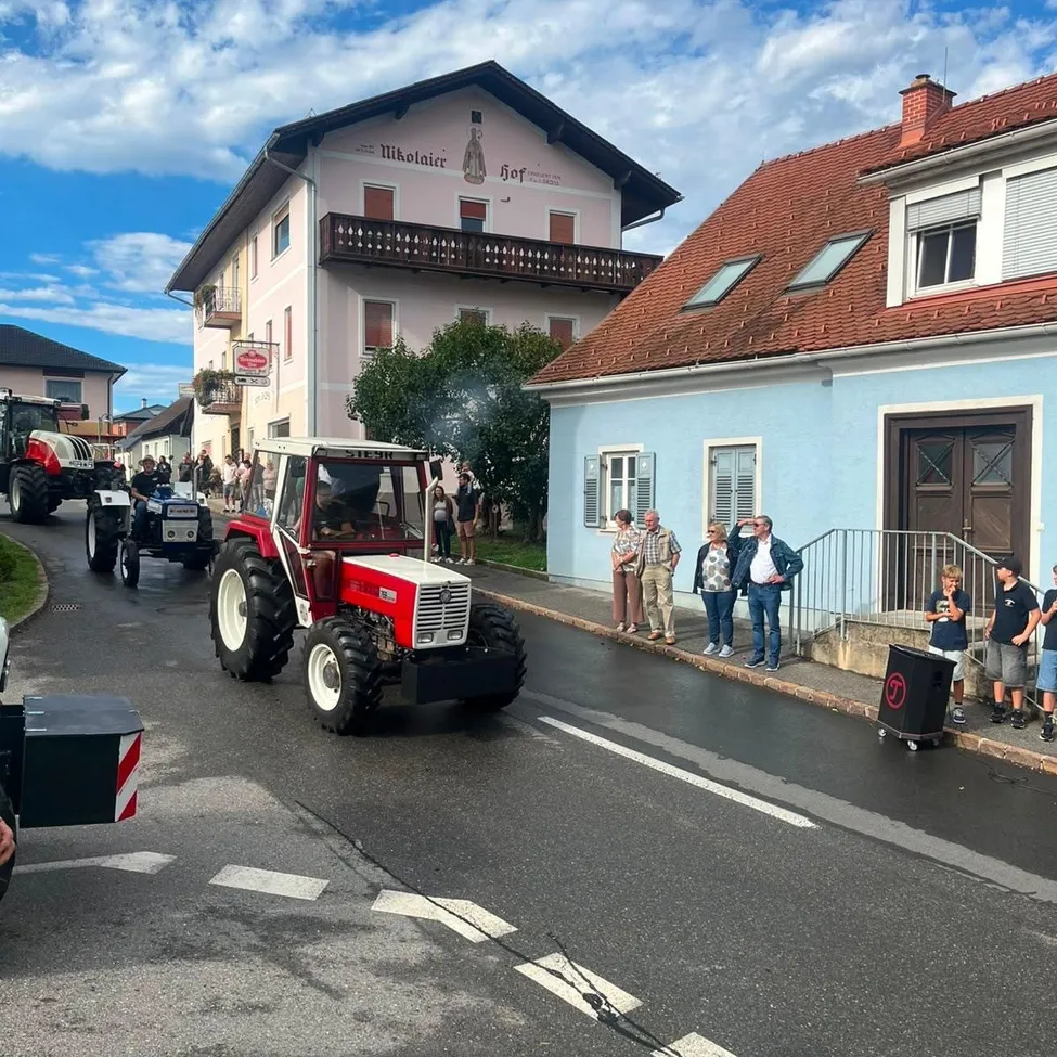 Ein Traktor-Parade mit mehreren Traktoren, die die Straße hinunterfahren, während Menschen vom Bürgersteig zusehen.