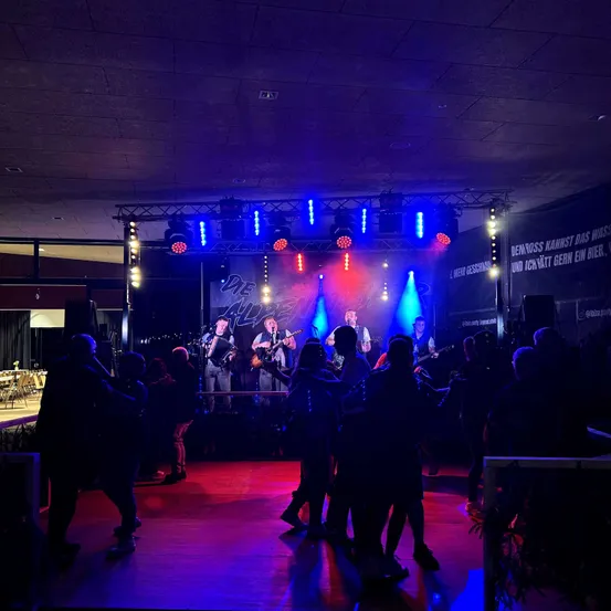 Eine Band spielt auf der Bühne mit roter und blauer Beleuchtung, während Menschen davor tanzen.