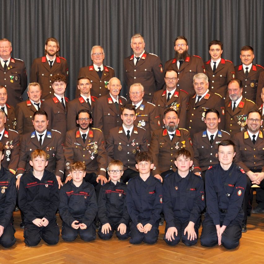 Eine Gruppe von Militäroffizieren und Kadetten posiert für ein Foto. Die Offiziere tragen Uniformen mit Medaillen, während die Kadetten schwarze Uniformen tragen. Sie alle lächeln und schauen in die Kamera.