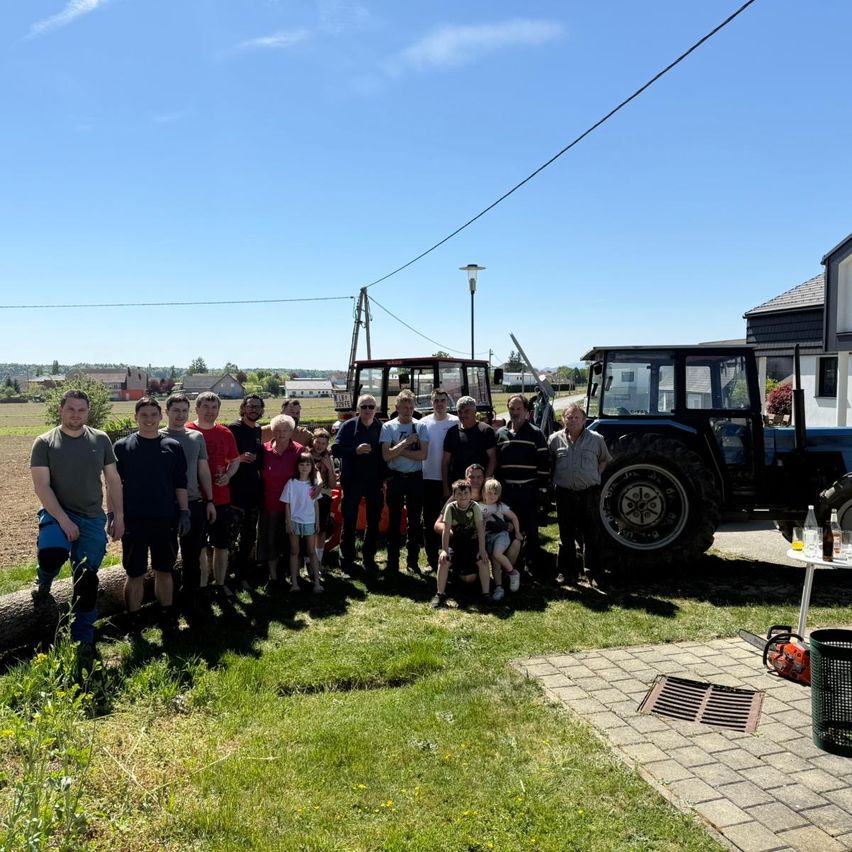 Eine Gruppe von Menschen in Freizeitkleidung posiert für ein Foto auf einem Feld mit Traktoren und einem klaren blauen Himmel.