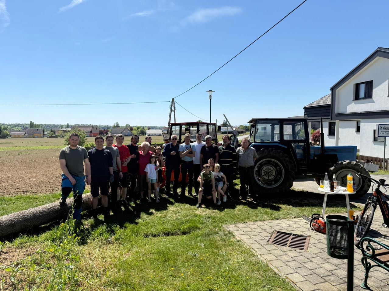 Eine Gruppe von Menschen in Freizeitkleidung posiert für ein Foto auf einem Feld mit Traktoren und einem klaren blauen Himmel.