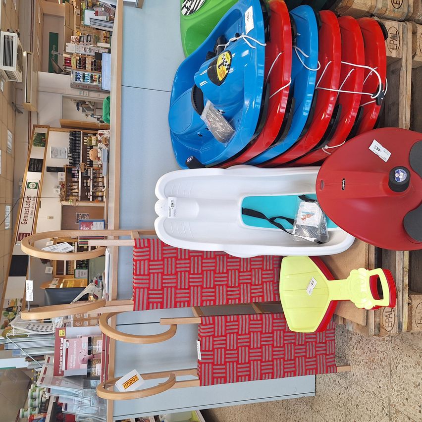 Ein Geschäft zeigt verschiedene Schlitten in mehreren Farben, darunter Blau, Rot und Weiß. Ein roter Schlitten ist rechts mit einem Preisschild. Ein weißer Schlitten befindet sich in der Mitte.