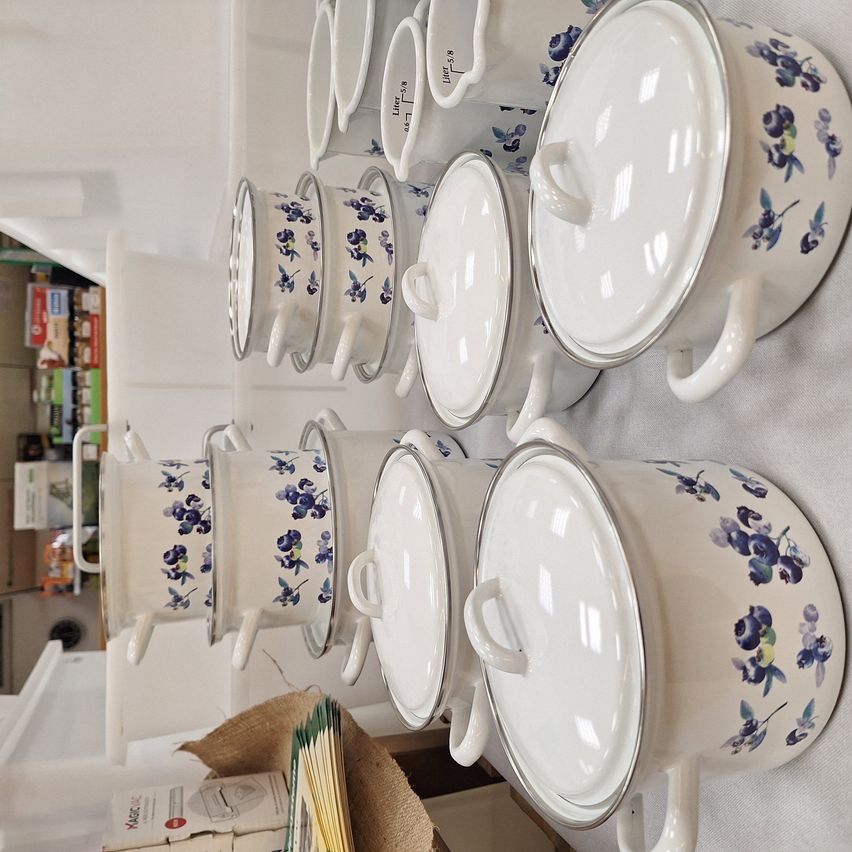 Multiple white ceramic pots with blue floral patterns are arranged in a row on a white surface. Each pot has a lid with a handle. A brown box with some yellow objects is at the bottom.