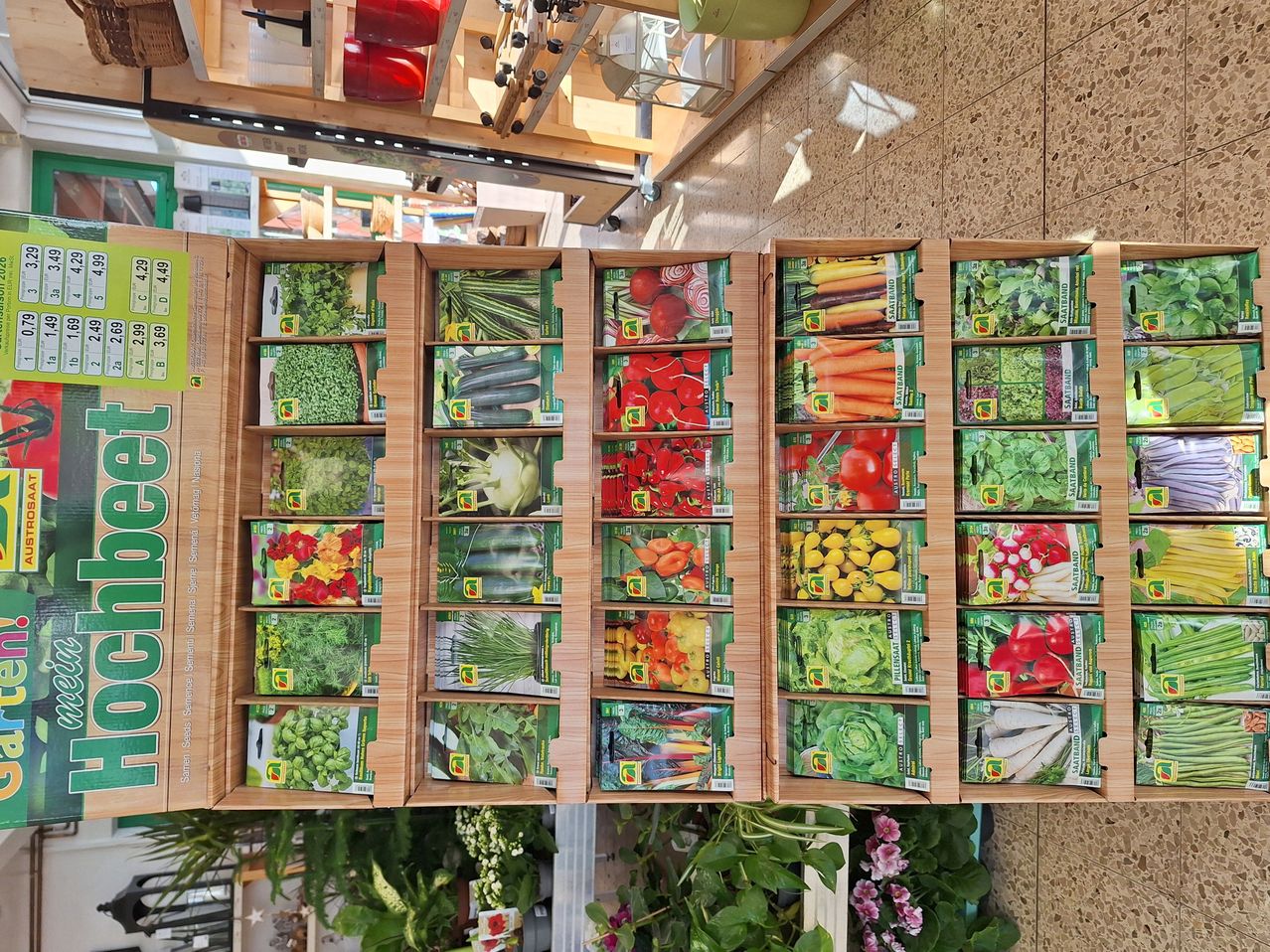 Wooden display with multiple packs of seeds, organized in rows. Each pack contains a variety of vegetable seeds, including tomatoes, cucumbers, and carrots.