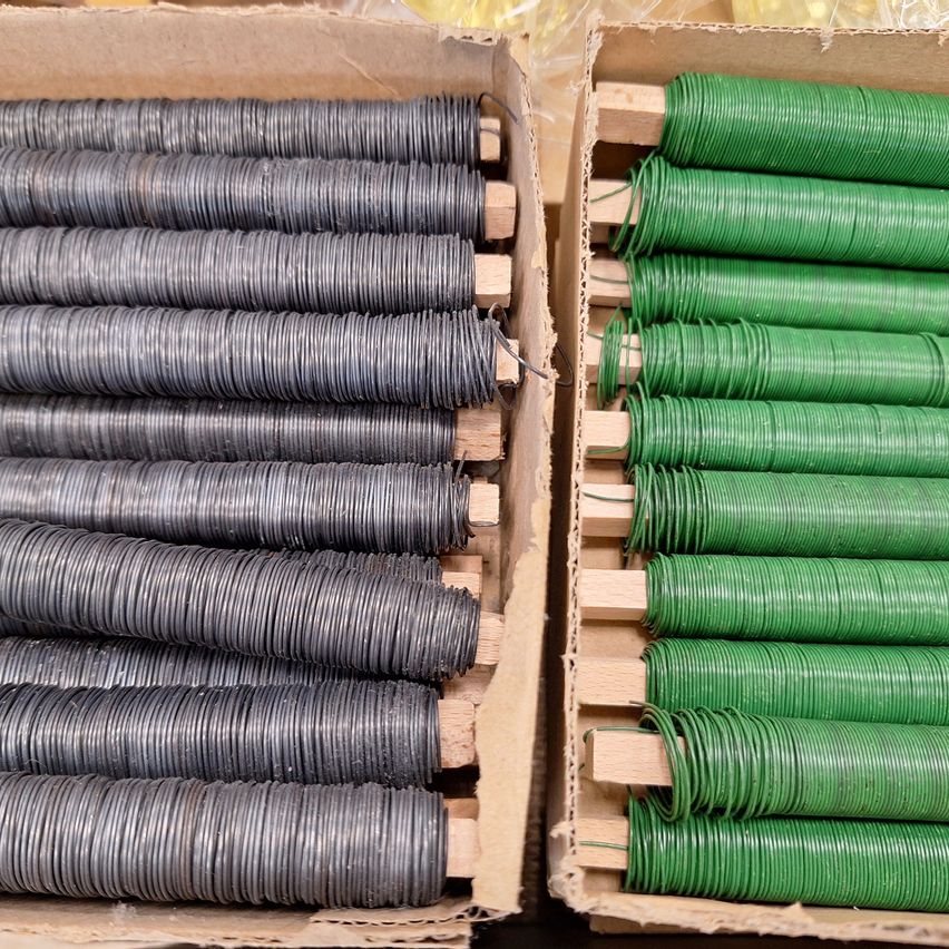 Two cardboard boxes containing coiled metal wires: one box with gray wires and the other with green wires. Both boxes have wooden dividers.