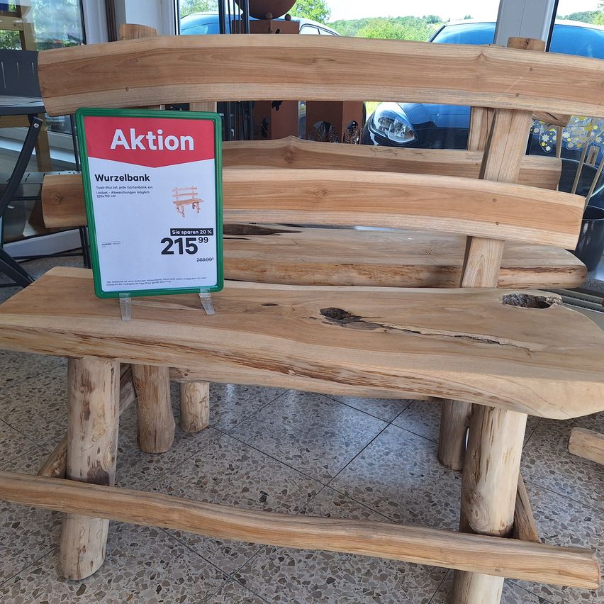A wooden bench is on display inside a store, with a red sign above it that reads 'Aktion'. The bench has a price tag of 215.99 euros and is 20% off.
