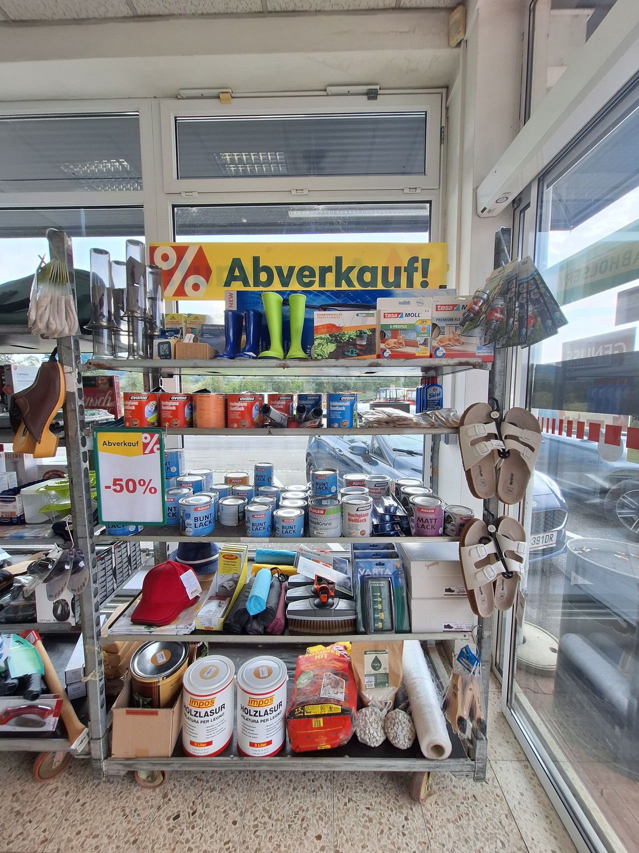 A store with a clearance sale sign, featuring a variety of items on shelves including boots, paint cans, and other household items.