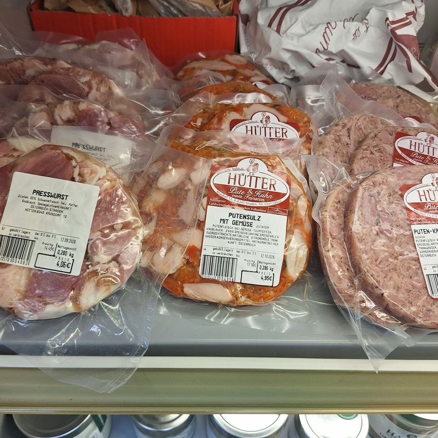 A close-up of various types of sausages in plastic packaging, including Presswurst, Putensulz mit Gemuse, and Puten-Krönung, displayed on a shelf.