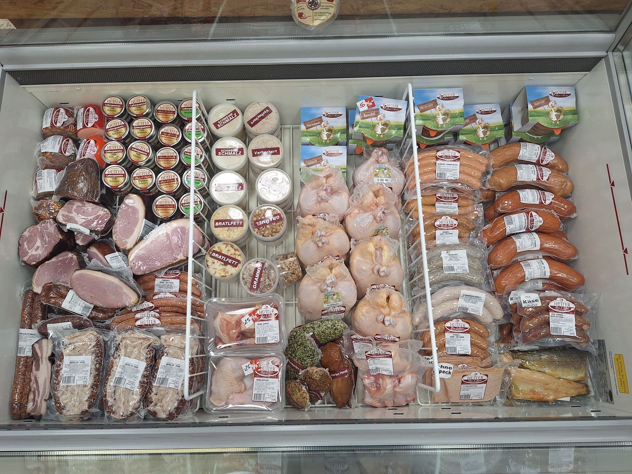 A refrigerated display case filled with various meats, sausages, and packaged products, all labeled with the brand name 'HUTTER'.