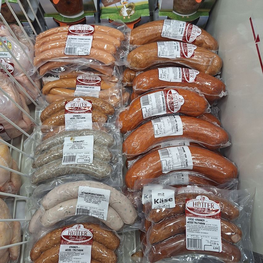 A display case filled with various types of sausages, all wrapped in plastic and labeled with the brand name Hutter. The sausages are in different colors and sizes, with some having white labels and others having red labels.
