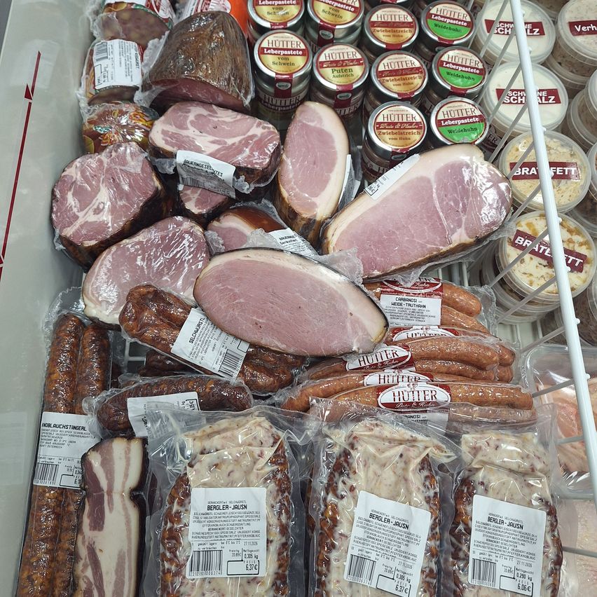 A close-up view of various packaged meats and sausages in a refrigerated display case. The meats include slices of ham, sausages, and other cured meats, all neatly arranged and labeled.