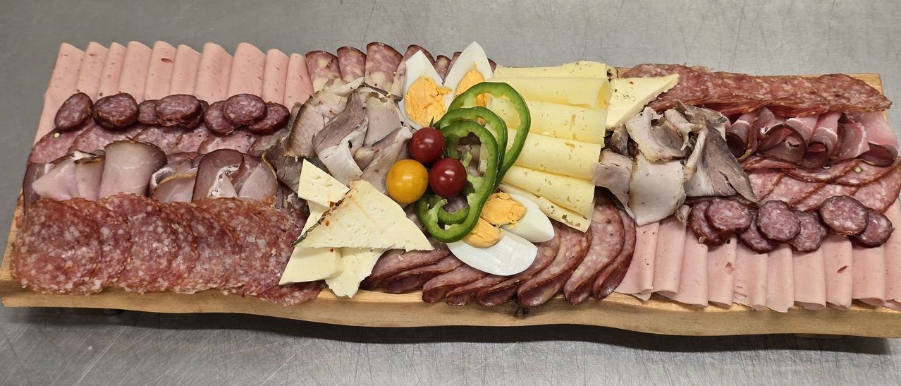 Ein Holztablett zeigt eine Auswahl an Fleisch, Käse, gekochten Eiern und Paprika. Verschiedene Fleischsorten sind links und rechts angeordnet, mit unterschiedlichen Käsesorten in der Mitte.