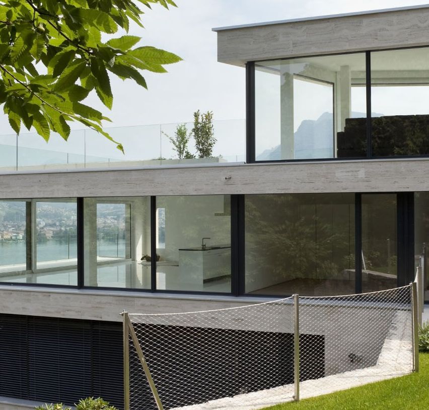 Modernes Haus mit Glaswänden und Balkon am Hang mit Blick auf das Wasser.