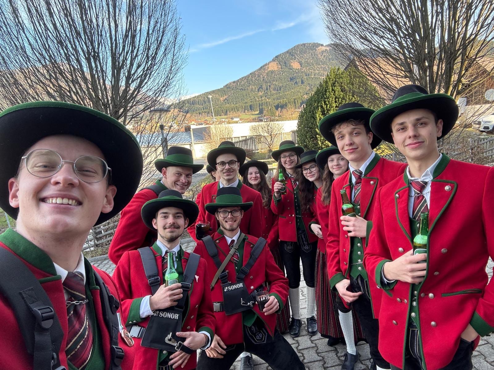 Eine Gruppe von Menschen in roter und grüner traditioneller Kleidung posiert für ein Foto mit Bergen im Hintergrund.