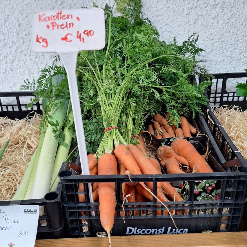 Eine Anzeige von Karotten und Lauch in schwarzen Kisten mit einem Preisschild, das 4,90 Euro pro Kilogramm anzeigt.