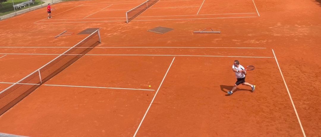 Ein Tennisspieler schwingt nach einem Ball auf einem Sandplatz. Der Platz hat weiße Linien und ein Netz.