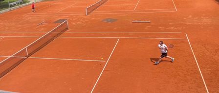 Ein Tennisplatz im Freien mit zwei Netzen und einem Spieler, der den Ball schlägt.