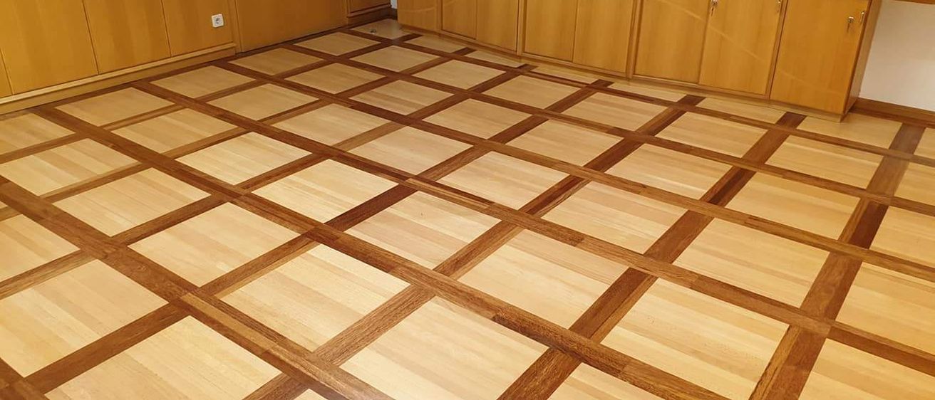 Ein Raum mit einem mit Quadraten und Rechtecken eingelegtem Holzboden und hölzernen Schränken an der Wand.