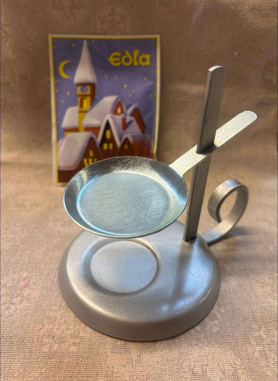 Ein silberner Löffel ruht auf einem Metallständer, ein Weihnachtskarten im Hintergrund. Löffel und Ständer haben eine reflektierende Oberfläche.