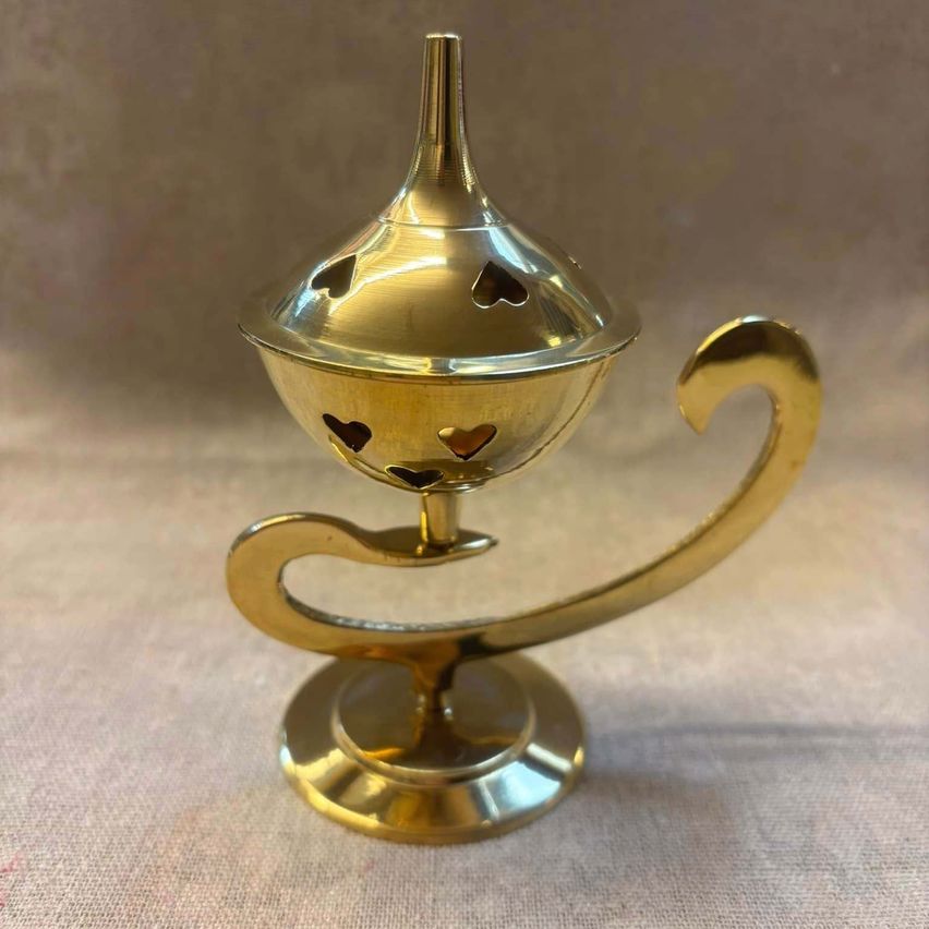 Ein kleiner, komplizierter Räucherbrenner aus Messing mit herzförmigem Design auf seiner Oberfläche, auf einem grauen Hintergrund platziert.