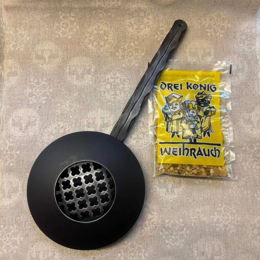 Ein schwarzer Räucherbrenner mit Gittermuster neben einer gelben Plastiktüte von 'Orel Konig Weihraucht'.