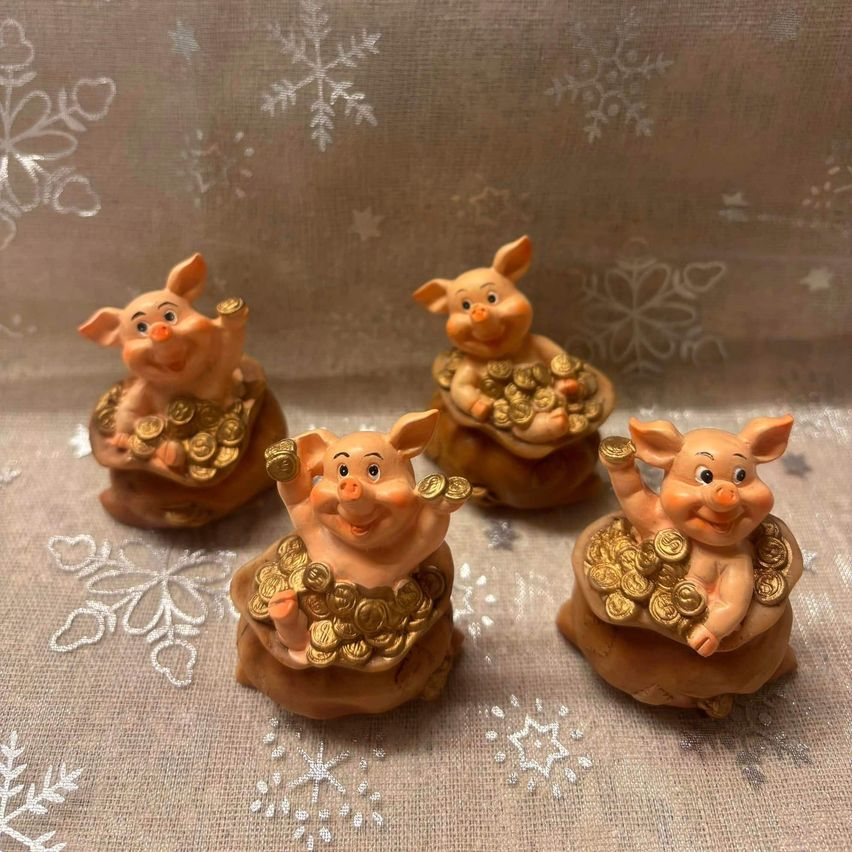 Vier kleine Keramik-Schweinefiguren mit goldenen Münzen auf einer strukturierten Oberfläche mit Schneeflockenmustern im Hintergrund.