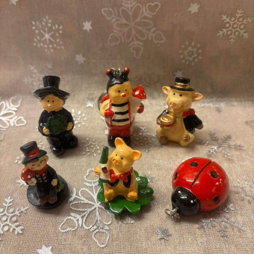 Sechs Keramikfiguren auf einem beigefarbenen Tuch mit Schneeflocken, einschließlich eines Mannes, eines Bären, eines Schweins, einer Marienkäferin und einer Marienkäferin mit schwarzen Punkten.