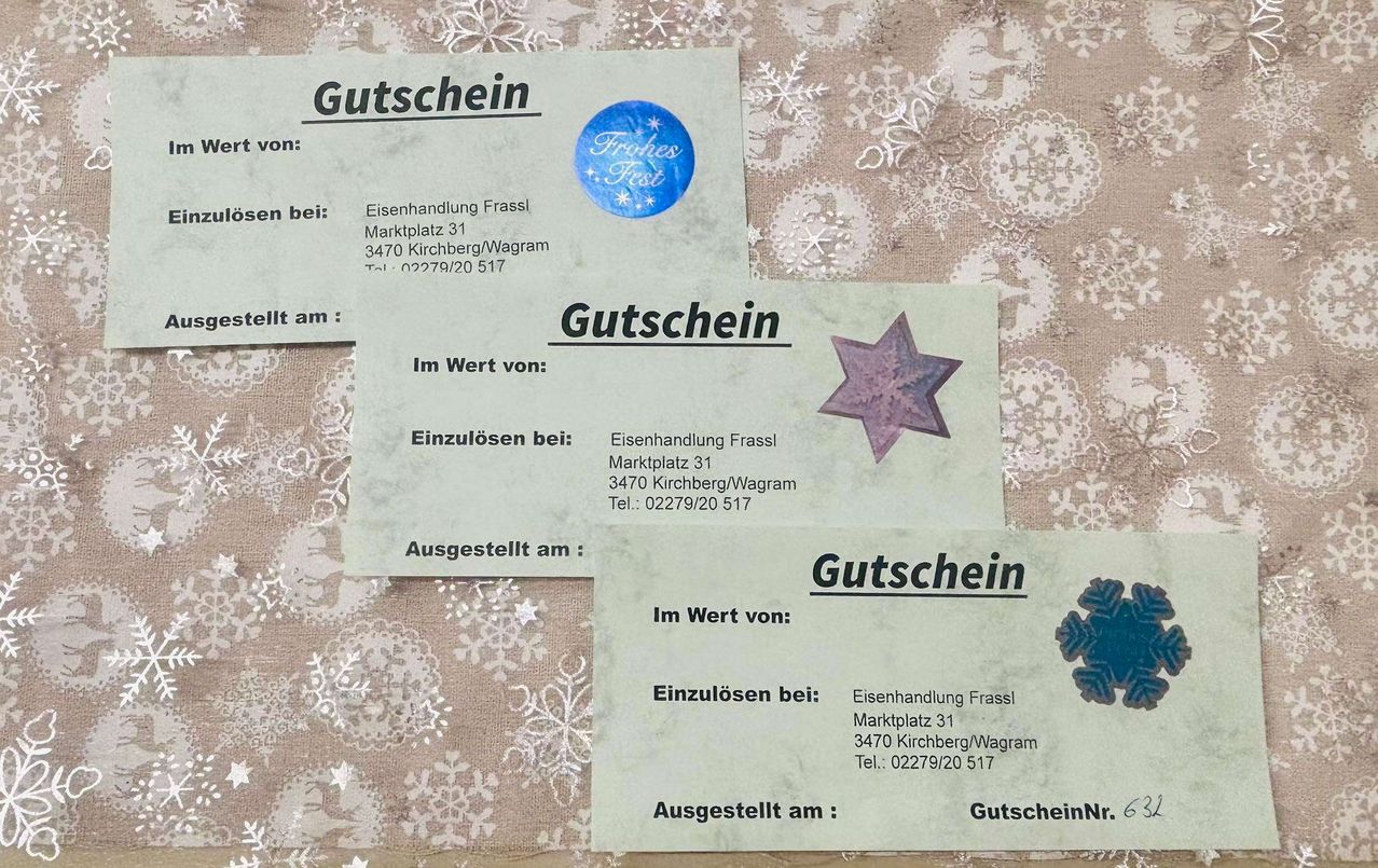 Drei Geschenkgutscheine eines Geschäfts namens Eisenhandlung Frassl liegen auf einem Tuch mit Schneeflocken. Die Gutscheine haben einen Wert, ein Datum und ein Sternsymbol. Die Adresse ist Marktplatz 31, 3470 Kirchberg/Wagram. Die Telefonnummer lautet 02279/20 517.