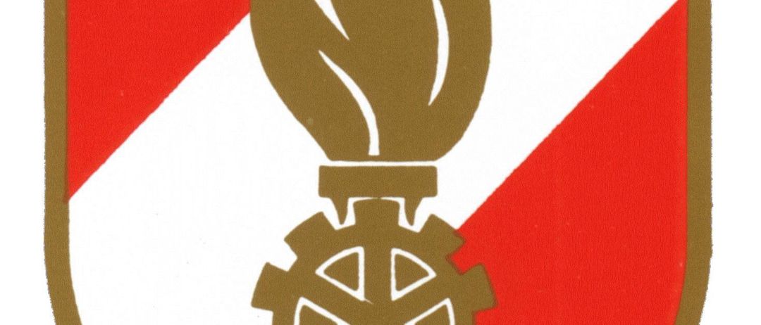 Ein rot-weißes Schild mit einer Flamme und einem Zahnradsymbol in der Mitte. Die Flamme ist gelb und gold, und das Zahnrad hat dreieckige Formen.