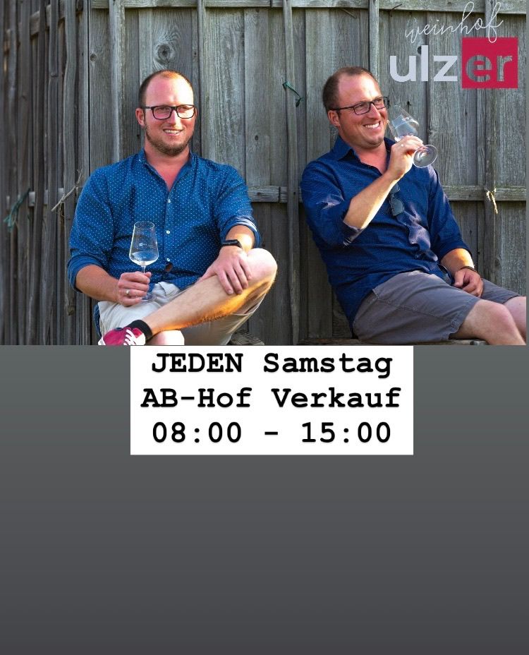 Zwei Männer sitzen nebeneinander auf einem Holzzaun und halten Weingläser in der Hand. Das Bild enthält den Text 'JEDEN Samstag AB-Hof Verkauf 08:00 - 15:00'.