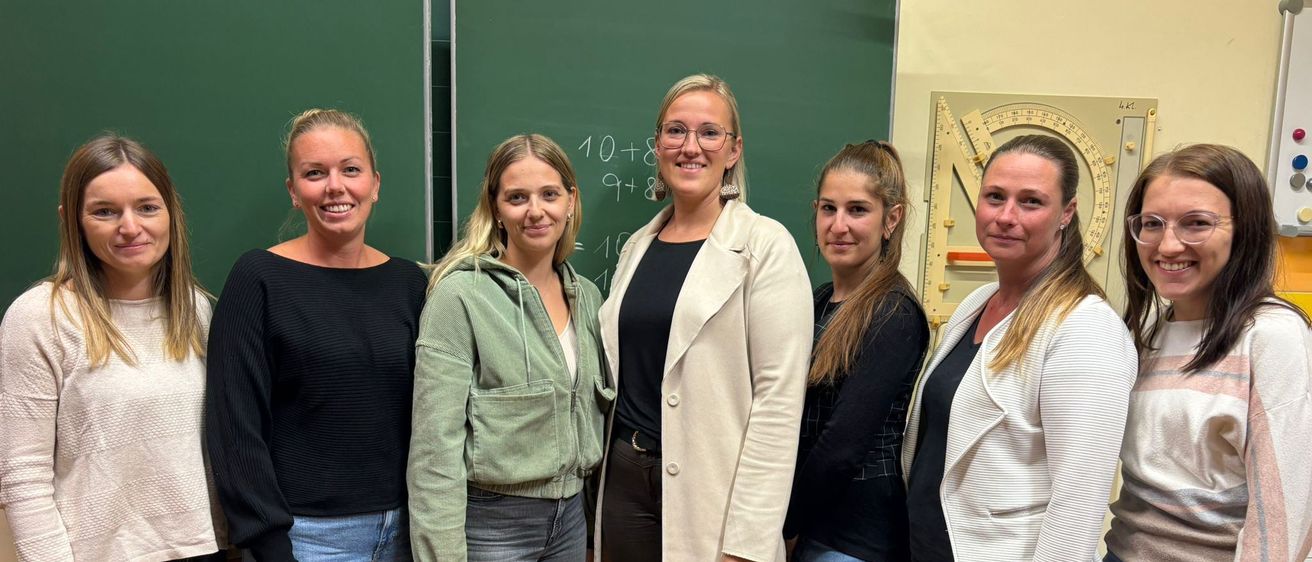 Eine Gruppe von Frauen steht vor einer Tafel mit mathematischen Gleichungen. Sie alle lächeln und scheinen für ein Foto zu posieren.