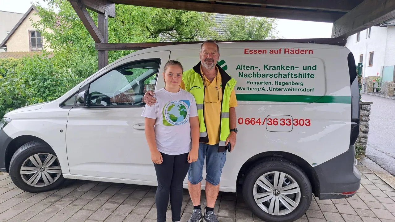 Ein Mann und ein junges Mädchen stehen neben einem weißen Van mit grüner und roter Beschriftung und posieren für ein Foto.
