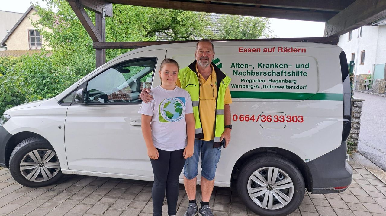 Ein Mann und ein junges Mädchen stehen neben einem weißen Van mit grüner und roter Beschriftung und posieren für ein Foto.