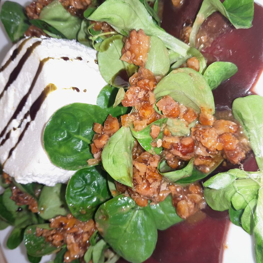 Ein Nahaufnahme eines Salatgerichts mit frischen Spinatblättern, karamellisierten Nüssen und einem cremigen weißen Käse mit geschwärztem Balsamico-Glasur.