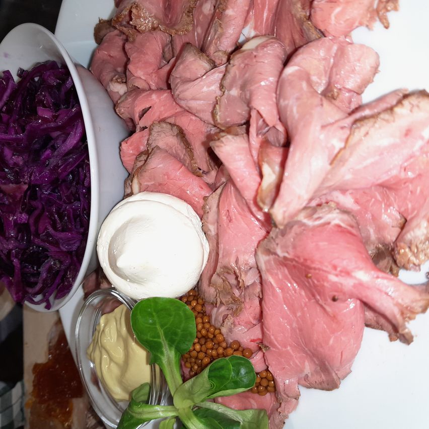 Ein weißer Teller enthält geschnittenes Fleisch mit Rotkohl und anderen Beilagen. Es gibt auch eine Schüssel mit Rotkohl und eine weiße Schüssel mit cremigem Käse und Senf.