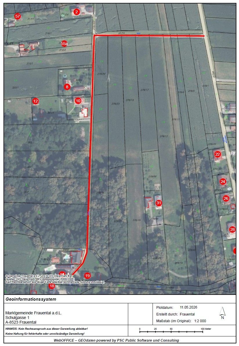 Eine Luftaufnahme zeigt ein Grundstück mit verschiedenen nummerierten Parzellen und einer roten Linie, die eine Straße anzeigt. Das Grundstück ist in kleinere Abschnitte unterteilt, die jeweils mit einer Nummer versehen sind. Bäume und Gebäude sind sichtbar, wobei die Straße durch das Grundstück verläuft.