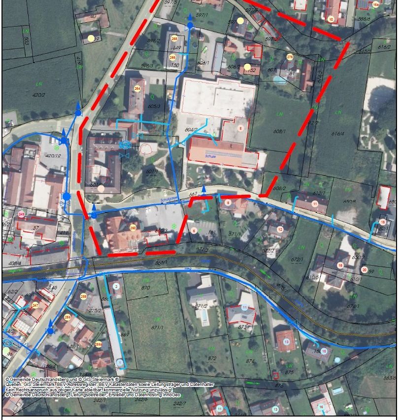 Die Karte zeigt verschiedene Wohn- und Gewerbegrundstücke mit nummerierten Parzellen. Blaue Linien repräsentieren Wasserleitungen, rote Linien Gasleitungen. Gebäude sind in verschiedenen Farben markiert. Die Karte enthält eine Legende, Maßstab und Nordanzeige.