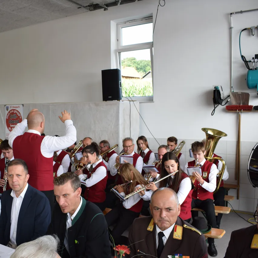 Eine Gruppe von Musikern, gekleidet in roten Westen, spielt verschiedene Instrumente in einem Raum. Ein erwachsener Mann in Anzug steht vorne und dirigiert die Band.