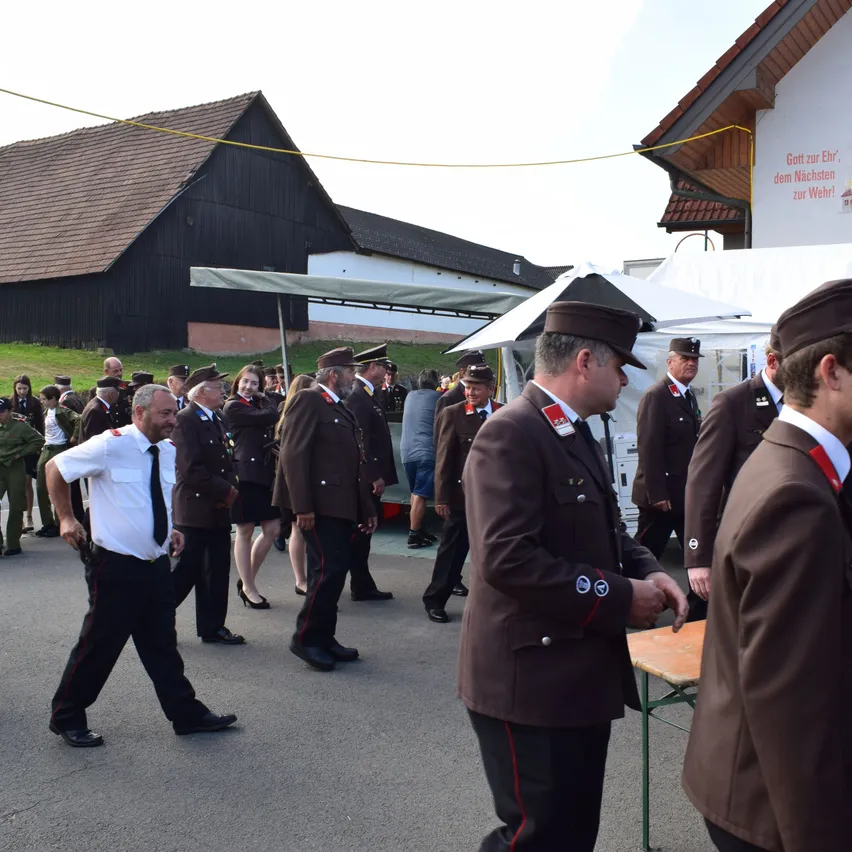 Eine Gruppe von Männern und Frauen in Uniform steht vor einem Gebäude. Einige tragen Hüte, andere sind in Zivilkleidung. Sie scheinen an einer Zeremonie teilzunehmen.