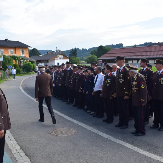 Eine Gruppe uniformierter Personen steht in Formation auf einer Straße, mit Gebäuden und Grünflächen im Hintergrund.