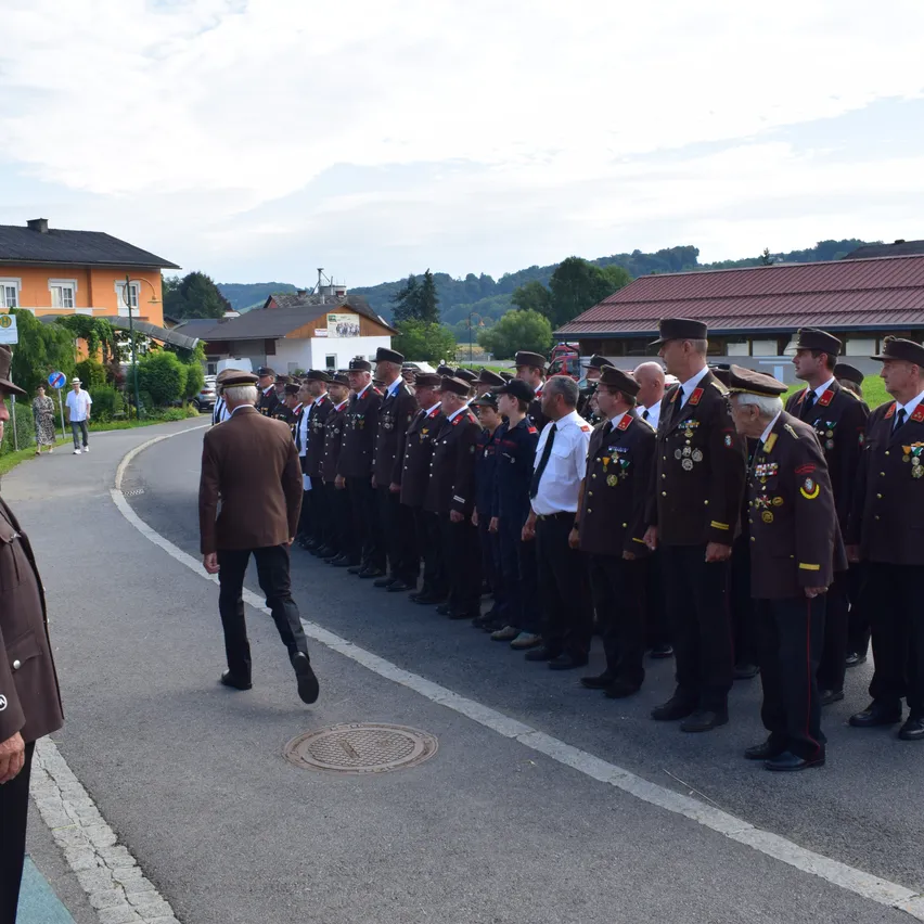 Eine Gruppe uniformierter Personen steht in Formation auf einer Straße, mit Gebäuden und Grünflächen im Hintergrund.