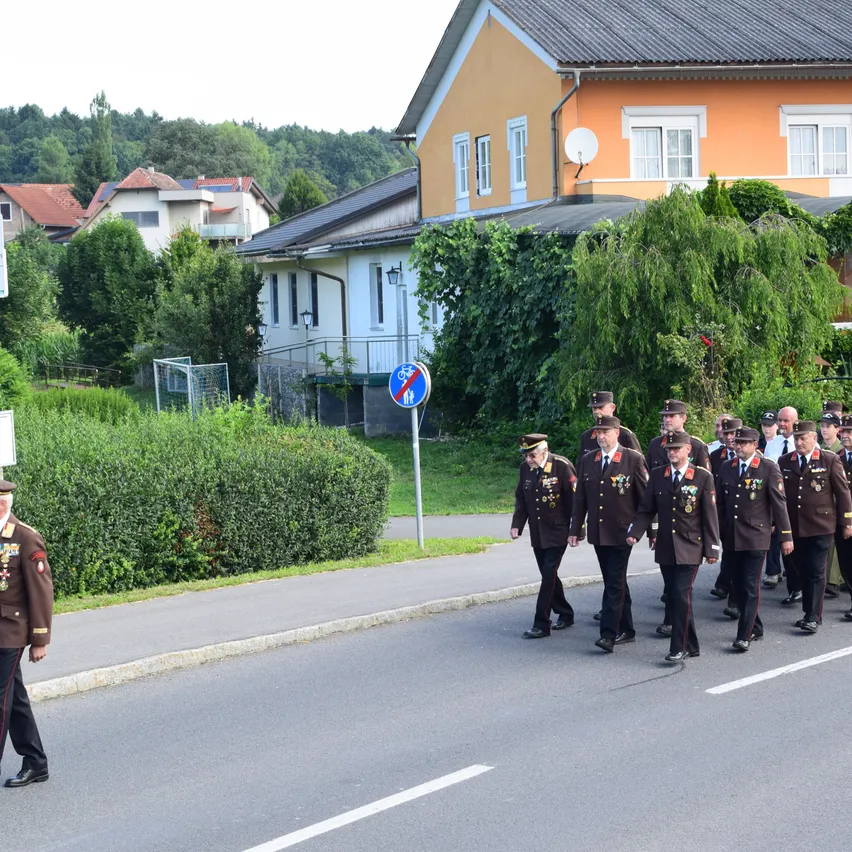 Eine Gruppe uniformierter Militäroffiziere marschiert auf einer Straße, ein Schild für kein Radfahren steht hinter ihnen. Bäume, Büsche und Gebäude sind im Hintergrund.