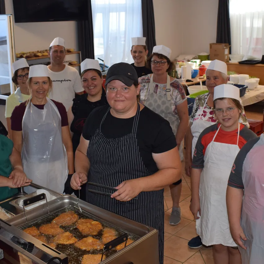 Eine Gruppe von Menschen in weißen Schürzen und Mützen steht in einer Küche und kocht Essen in einer Fritteuse.