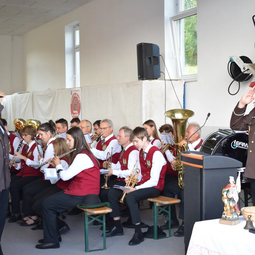 Eine Band spielt in einem Raum mit Trommel, Trompeten und Flöten. Ein Mann salutiert vor der Band.