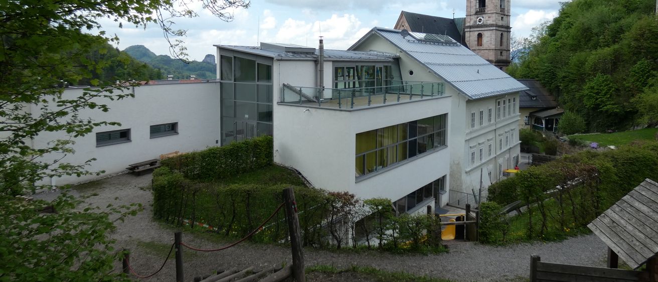 Ein weisses Gebäude mit modernem Design und Glasfenstern steht vor einer Kirche mit einem Turm.