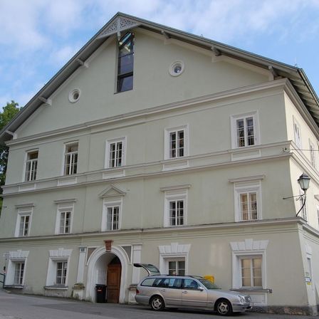 Ein zweistöckiges weißes Gebäude mit vielen Fenstern und einem Auto davor.