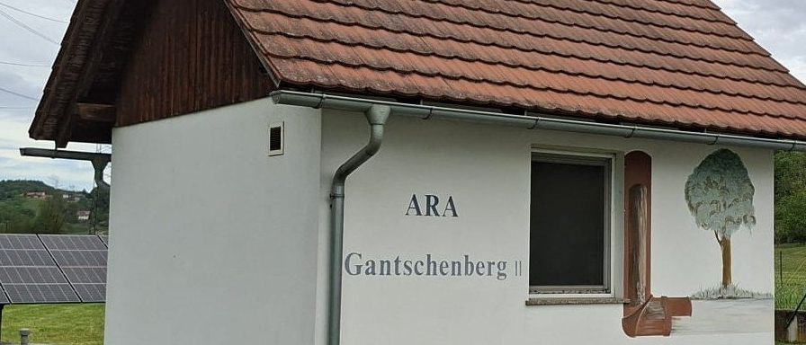 Ein kleines weißes Gebäude mit einem braunen Dach und dem Wort ARA darauf. Das Dach ist geneigt. Es gibt ein Fenster mit einem Baum auf der Seite gemalt.