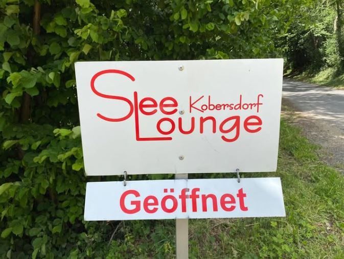 Ein Schild in Englisch und Deutsch, 'Slee Lounge Kobersdorf' ist oben und 'Geoffnet' ist unten.