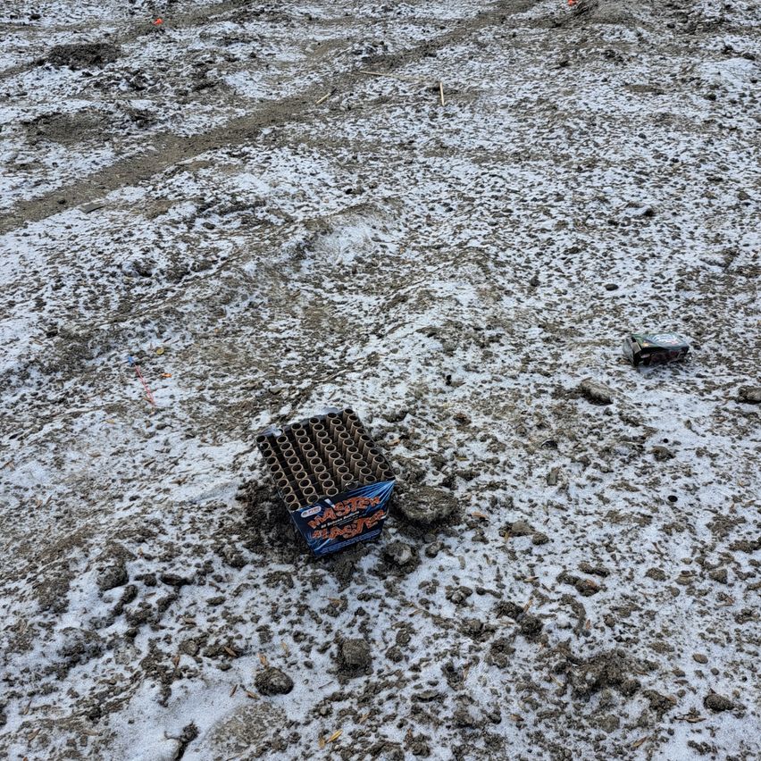 Eine offene Kiste mit Feuerwerkskörpern liegt auf dem mit Schnee bedeckten Boden. Ein weiteres kleines Objekt befindet sich in der Nähe.