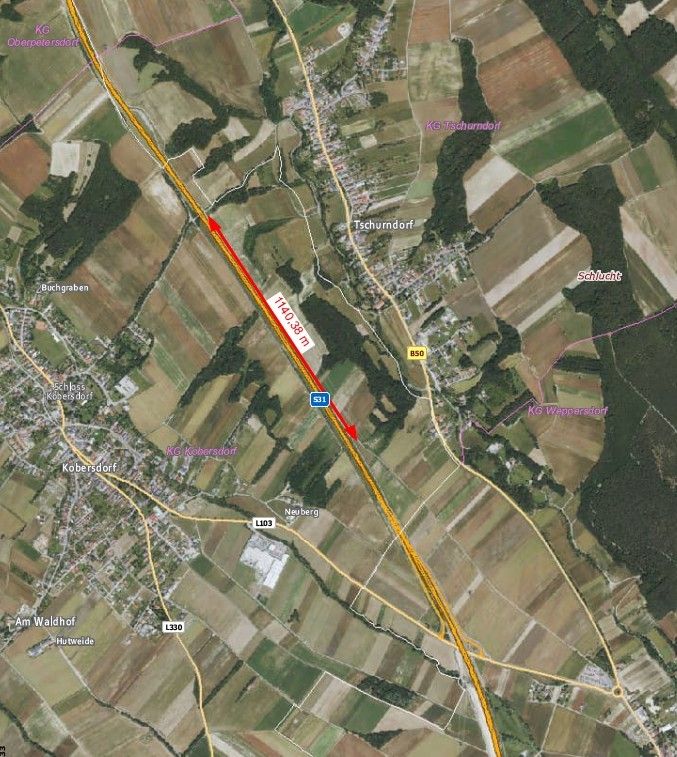 Eine Luftaufnahme zeigt die Straße mit der Bezeichnung L103, mit zwei roten Pfeilen, die auf die Stadt Kobersdorf zeigen. Mehrere andere Straßen und Dörfer sind sichtbar, einige davon sind beschriftet.